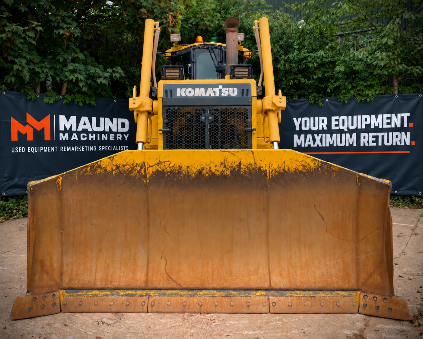 Front-facing Komatsu dozer in a yard with Maund Machinery banners